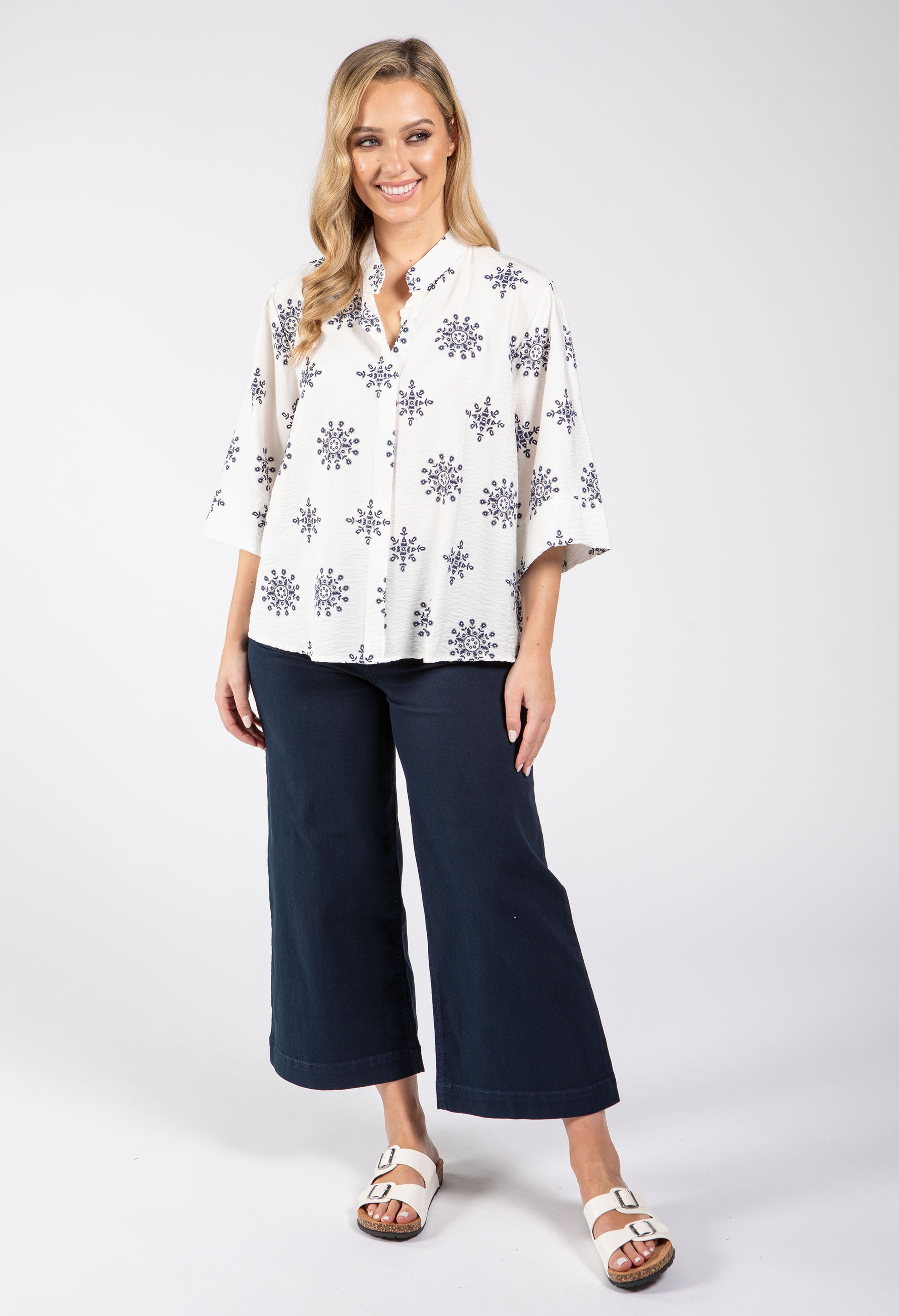 Woman wearing a white blouse with black floral patterns and navy blue pants on a white background