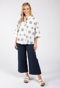 Woman wearing a white blouse with black floral patterns and navy blue pants on a white background