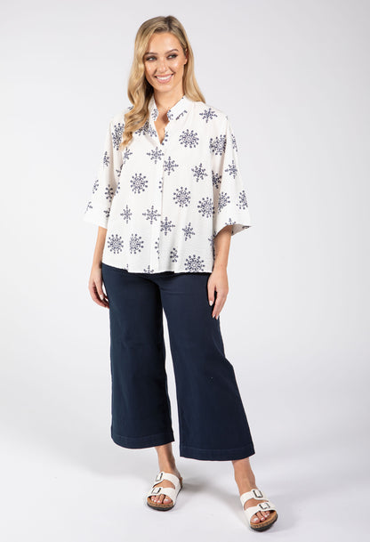 Woman wearing a white blouse with black floral patterns and navy blue pants on a white background