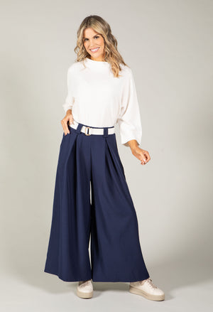 Woman wearing a white blouse and navy wide-leg pants on a plain background
