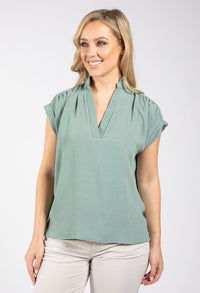 Woman wearing a light green blouse with cap sleeves on a white background