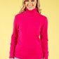 Woman wearing a bright pink turtleneck sweater against a yellow background