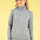 Woman wearing a gray turtleneck sweater against a yellow background