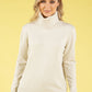 Woman wearing a cream turtleneck sweater against a yellow background