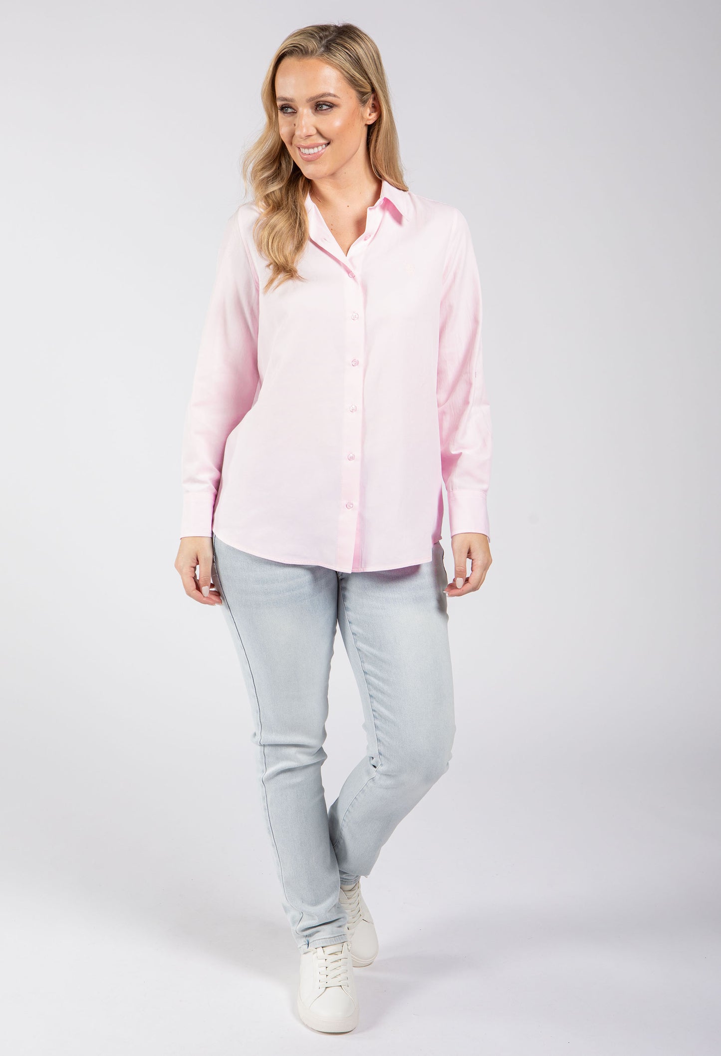 Woman wearing a pink shirt and light blue jeans on a white background