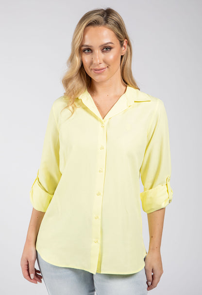 Woman wearing a light yellow blouse with rolled-up sleeves on a gray background