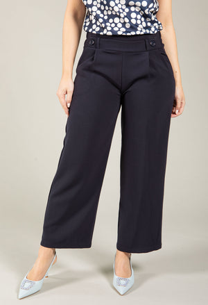Person wearing navy blue pants with a patterned top on a neutral background