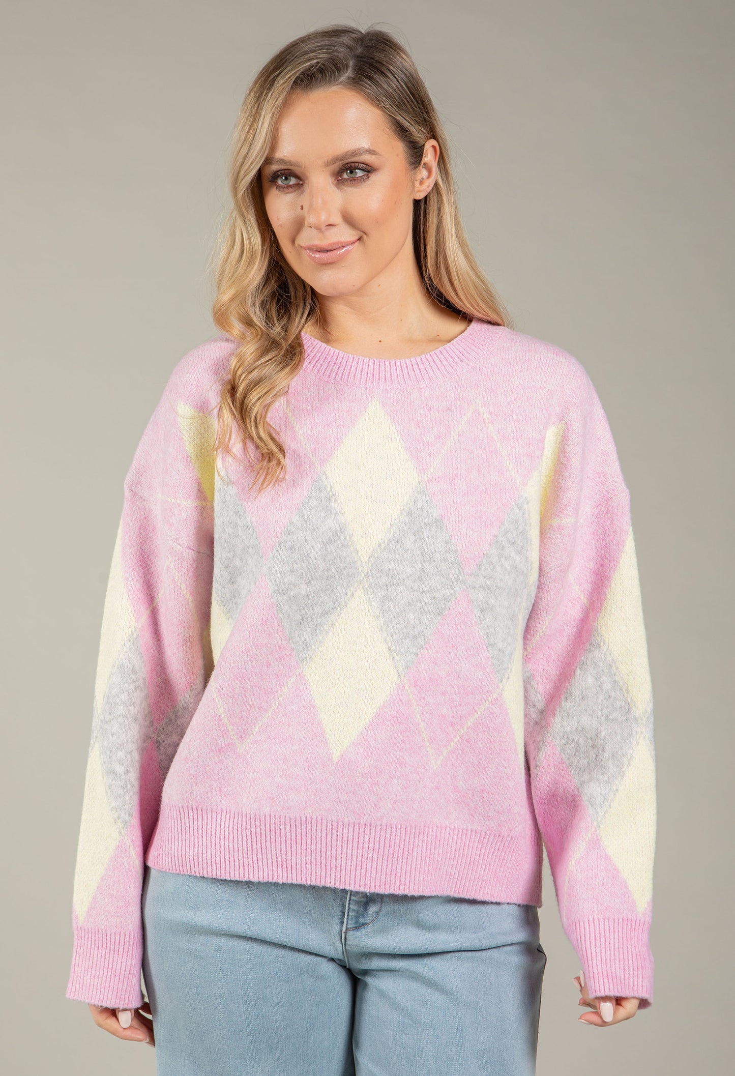 Woman wearing a pink, gray, and yellow diamond pattern sweater against a neutral background