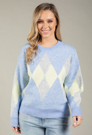 Woman wearing a light blue sweater with diamond pattern on a neutral background