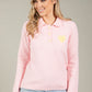Woman wearing a pink sweater with yellow buttons and a heart design on a gray background