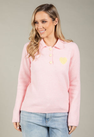 Woman wearing a pink sweater with yellow buttons and a heart design on a gray background