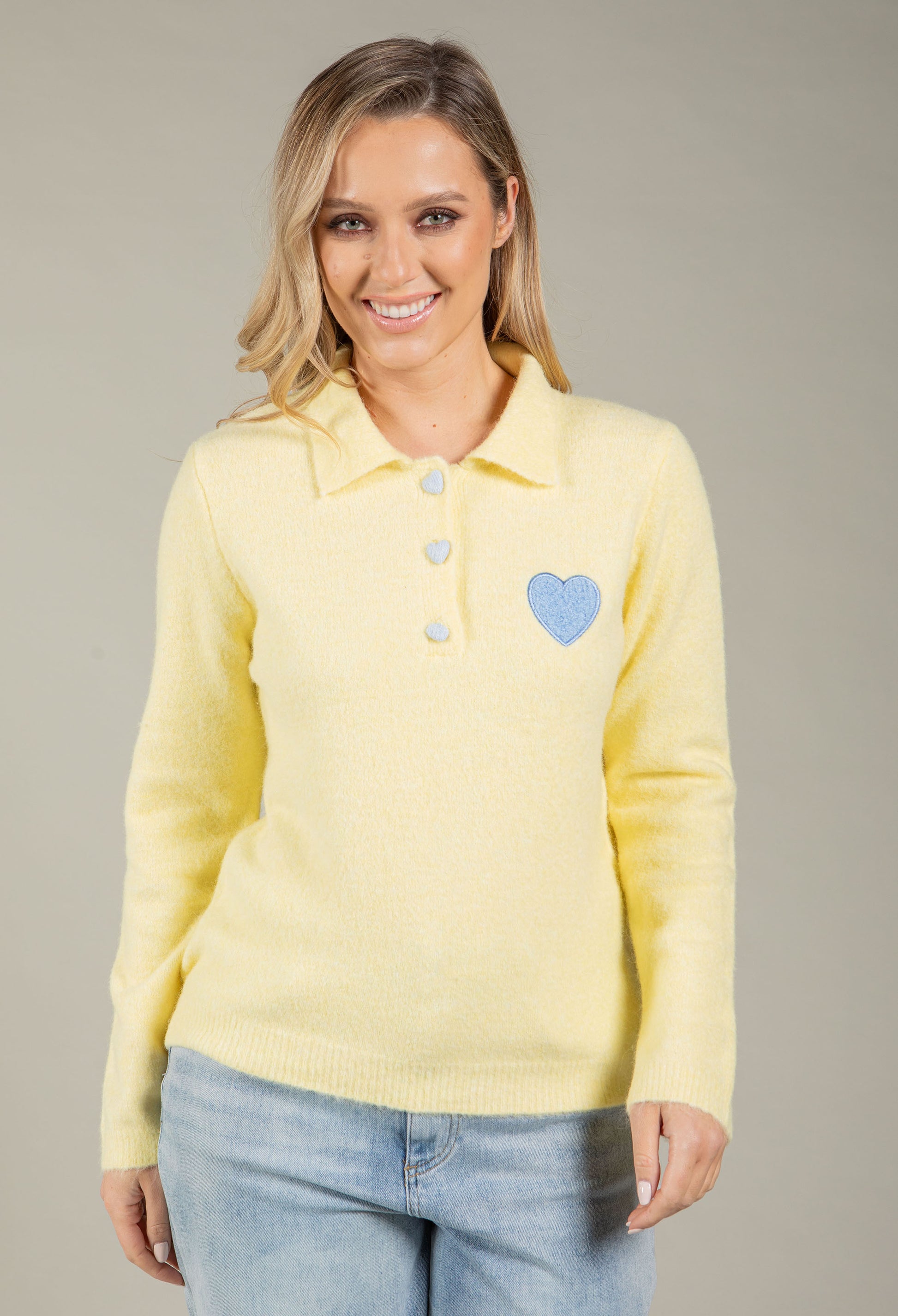 Woman wearing a yellow sweater with a blue heart design on a gray background
