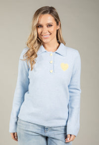 Woman wearing a light blue sweater with a yellow heart emblem on a beige background