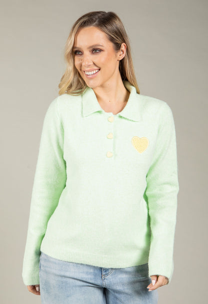 Woman wearing a light green sweater with a heart design on a gray background