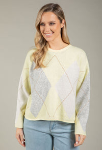 Woman wearing a light yellow sweater with gray diamond pattern on a plain background