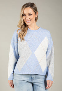Woman wearing a light blue and gray diamond pattern sweater against a neutral background
