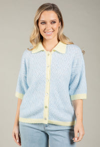 Woman wearing a light blue cardigan with yellow trim against a gray background