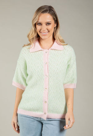 Woman wearing a light green cardigan with pink trim on a gray background