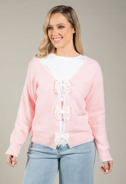 Woman wearing a pink sweater with decorative bows on a plain background