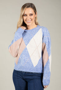 Woman wearing a blue sweater with diamond pattern on a plain background