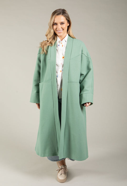 Woman wearing a long light blue coat over a striped shirt on a plain background