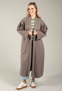 Woman wearing a long brown coat over a striped shirt on a plain background