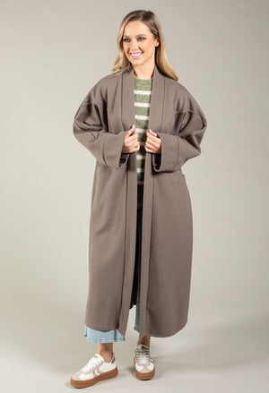 Woman wearing a long brown coat over a striped shirt on a plain background