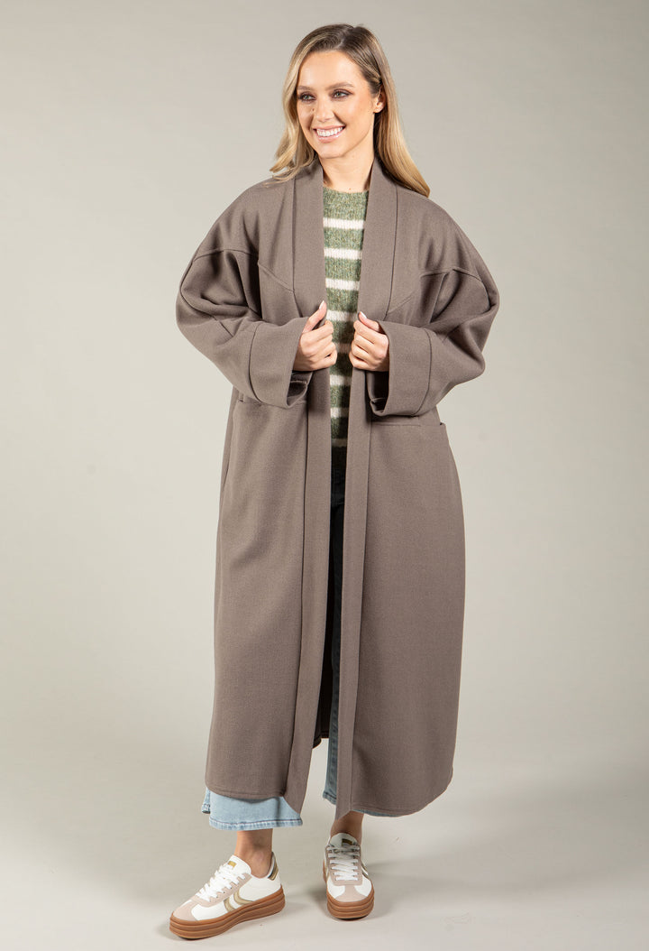 Woman wearing a long brown coat over a striped shirt on a plain background