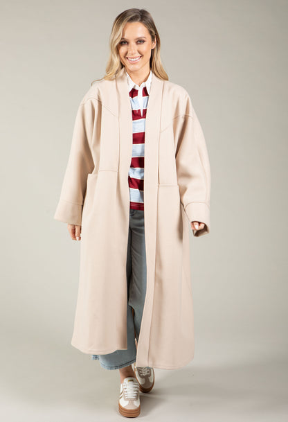 Woman wearing a long beige coat over a striped sweater on a plain background