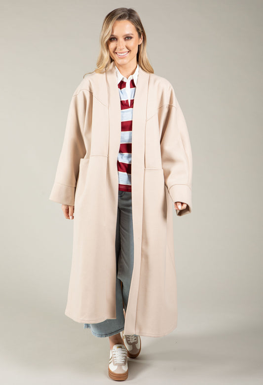 Woman wearing a long light blue coat over a striped shirt on a plain background