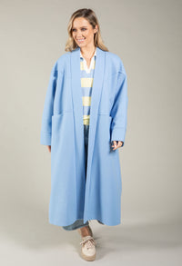 Woman wearing a long light blue coat over a striped shirt on a plain background