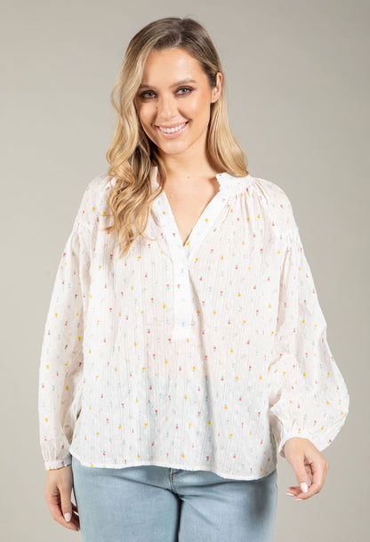 Woman wearing a white blouse with small patterns on a plain background