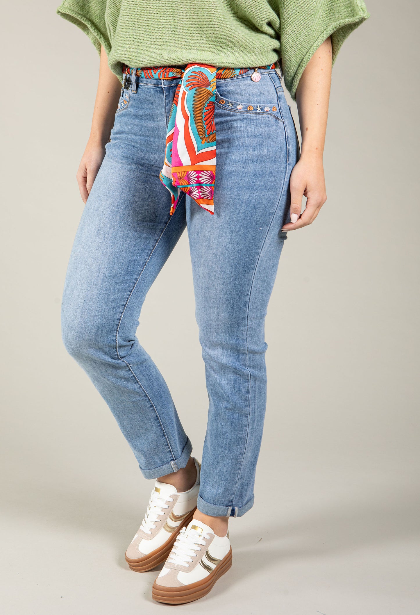 Person wearing blue jeans with a colorful bandana around the waist on a neutral background