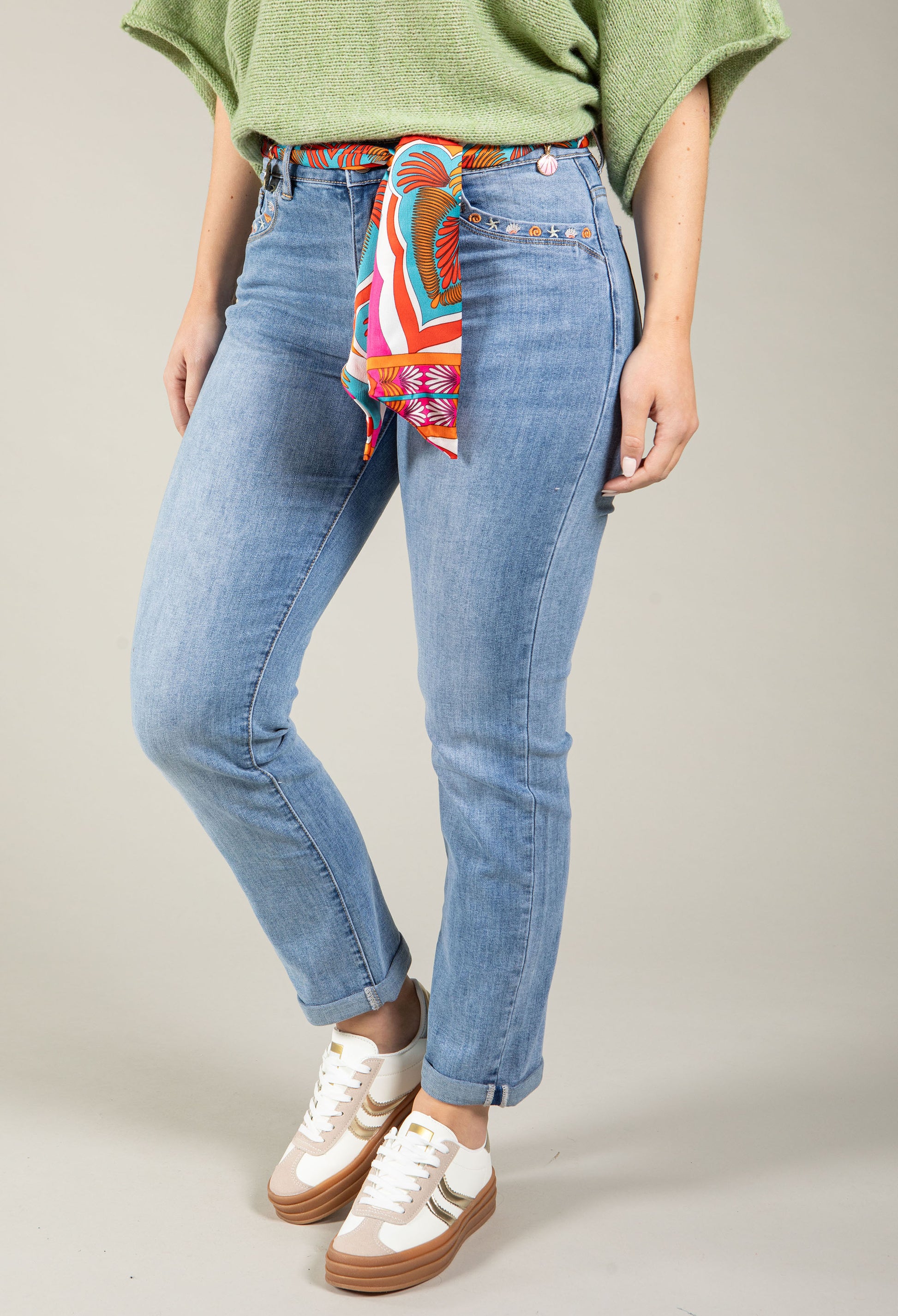 Person wearing blue jeans with a colorful bandana around the waist on a neutral background