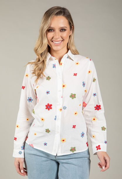 Woman wearing a white blouse with colorful floral patterns on a plain background