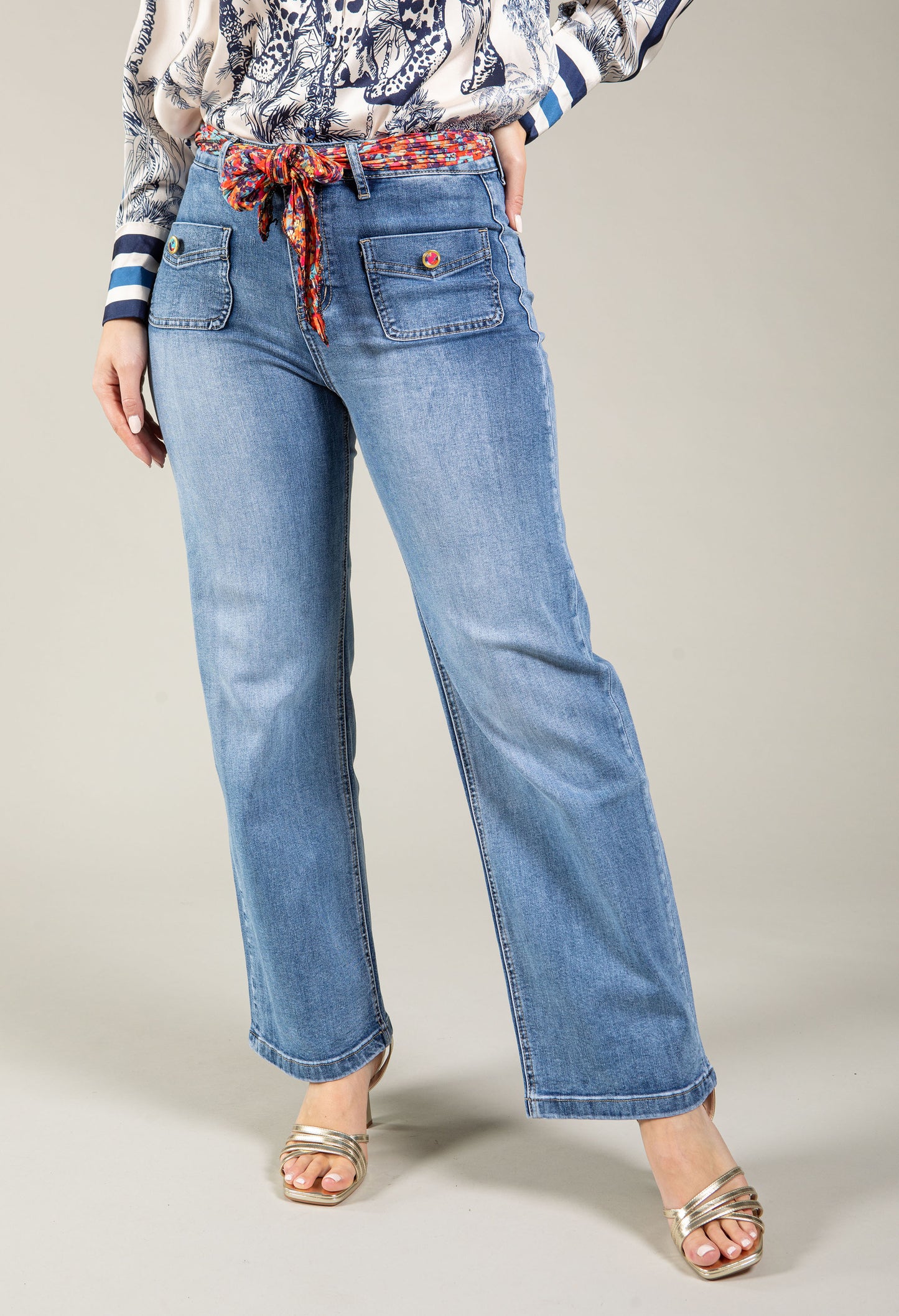 Person wearing blue jeans with a patterned belt on a neutral background
