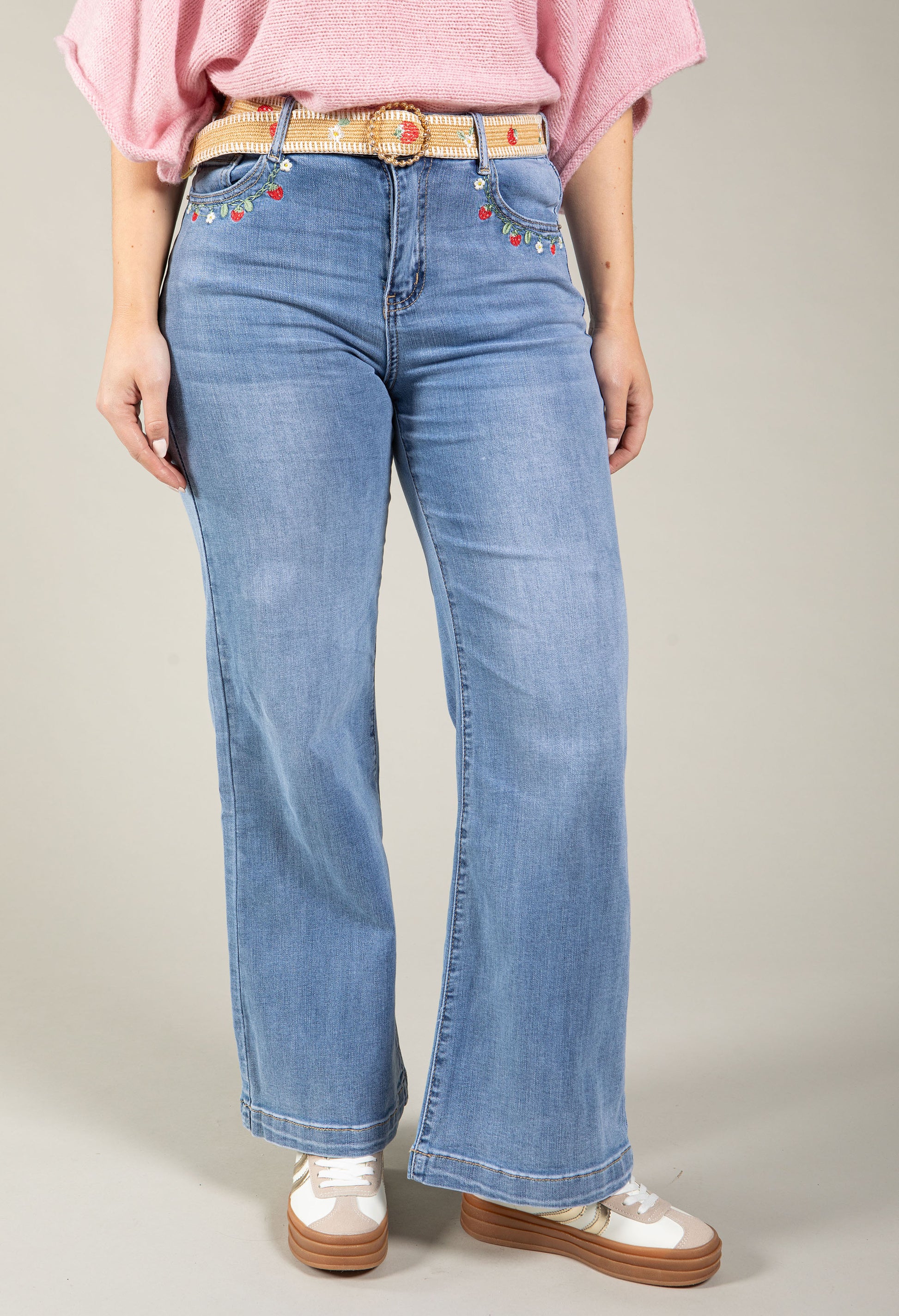 Person wearing blue jeans with decorative belt and pink top on a neutral background