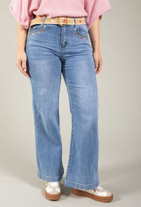 Person wearing blue jeans with decorative belt and pink top on a neutral background