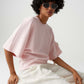 Person wearing a pink top and white pants sitting on a white chair against a plain background