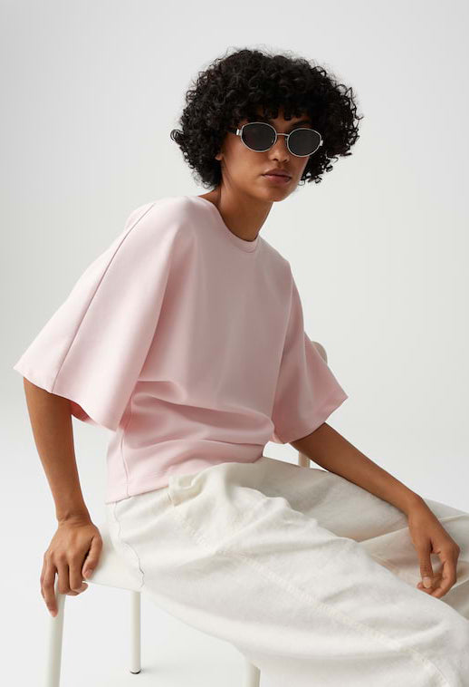 Person wearing a pink top and white pants sitting on a white chair against a plain background