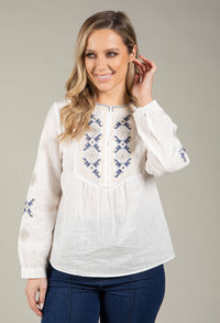 Woman wearing a white blouse with blue embroidery against a gray background