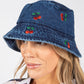 Woman wearing a denim bucket hat with cherry designs on a white background