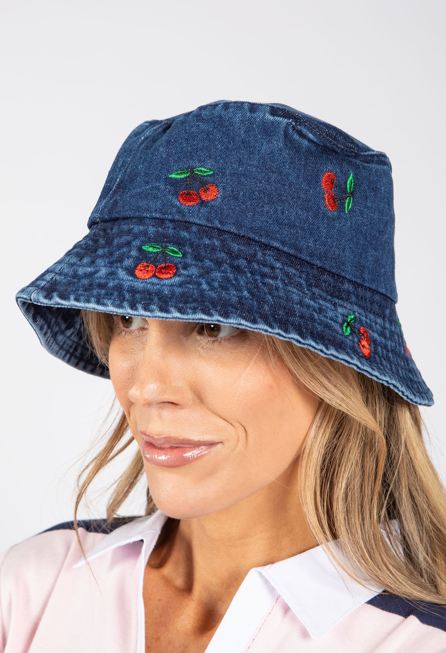 Woman wearing a denim bucket hat with cherry designs on a white background