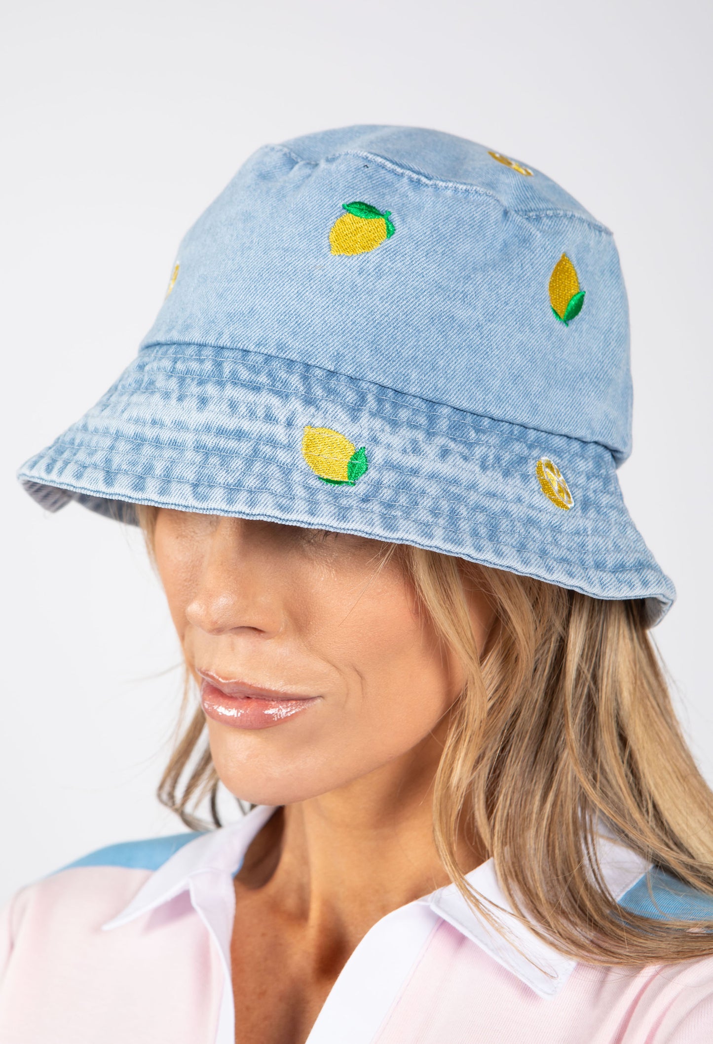 Light blue denim bucket hat with lemon designs worn by a person on a white background