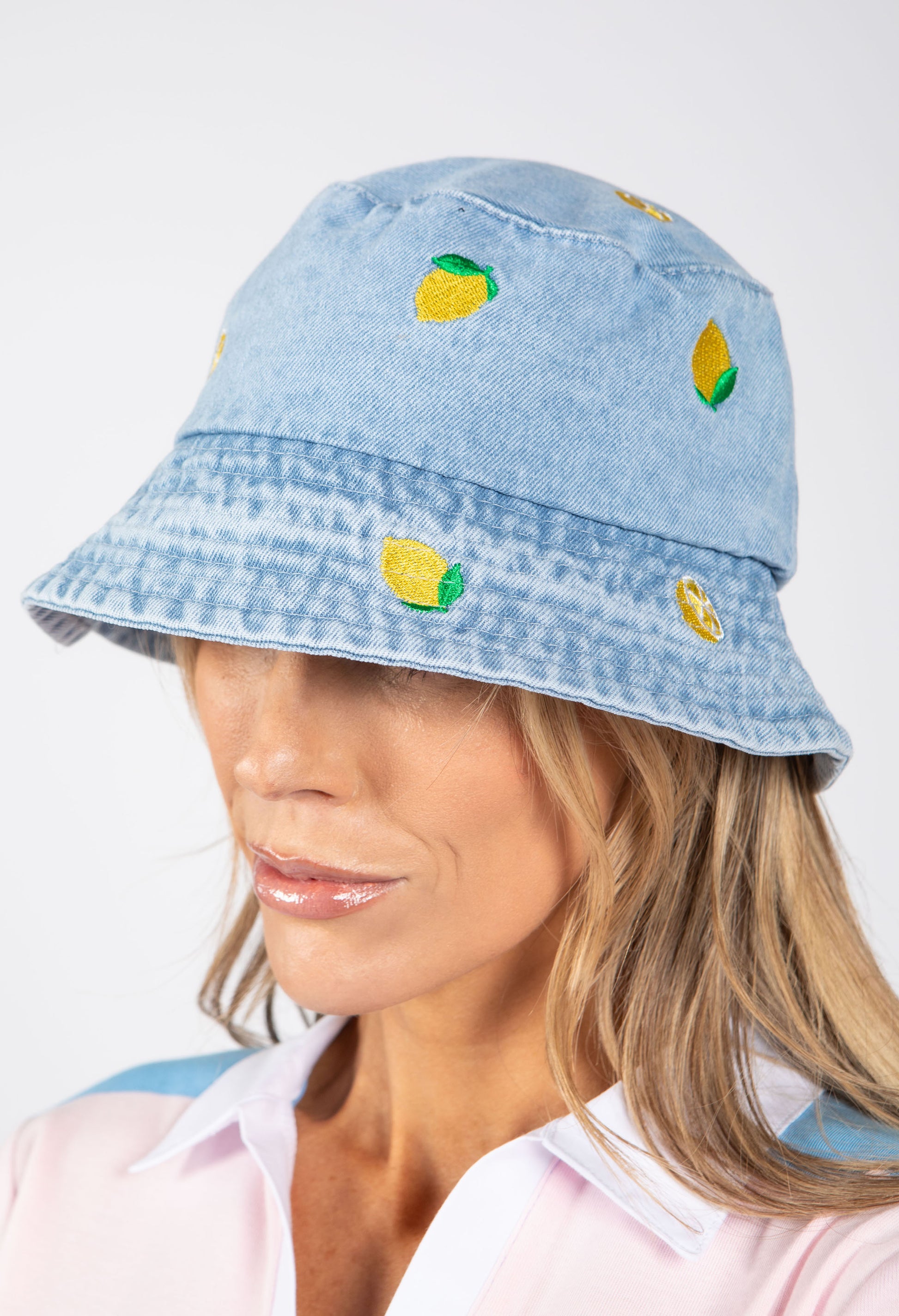 Light blue denim bucket hat with lemon designs worn by a person on a white background