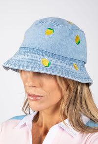 Light blue denim bucket hat with lemon designs worn by a person on a white background