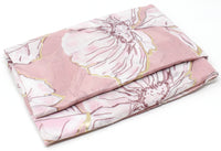 Folded pink floral blanket with white and gold accents on a white background