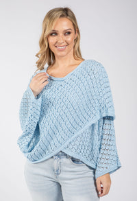 Woman wearing a light blue knitted poncho against a white background