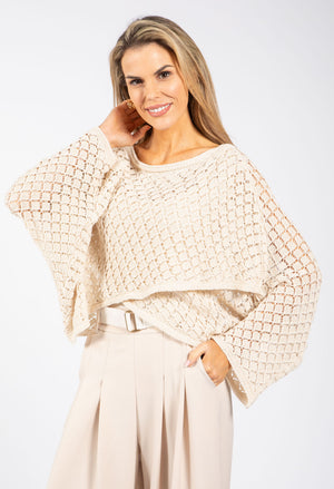 Woman wearing a beige knit poncho and pants on a white background