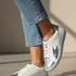 White sneakers with silver accents worn with blue jeans on a neutral background